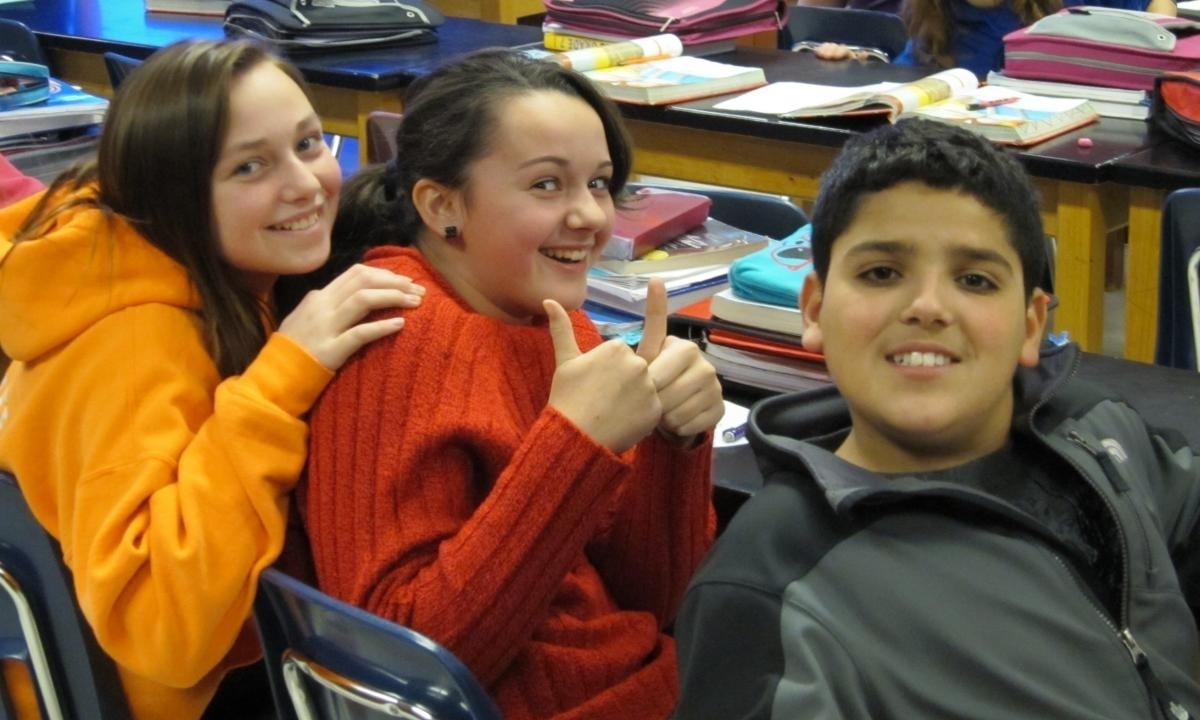Three students posing in a classroom setting, smiling at the camera.
