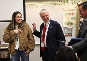 woman in brown jacket receiving award from man in black suit with red tie