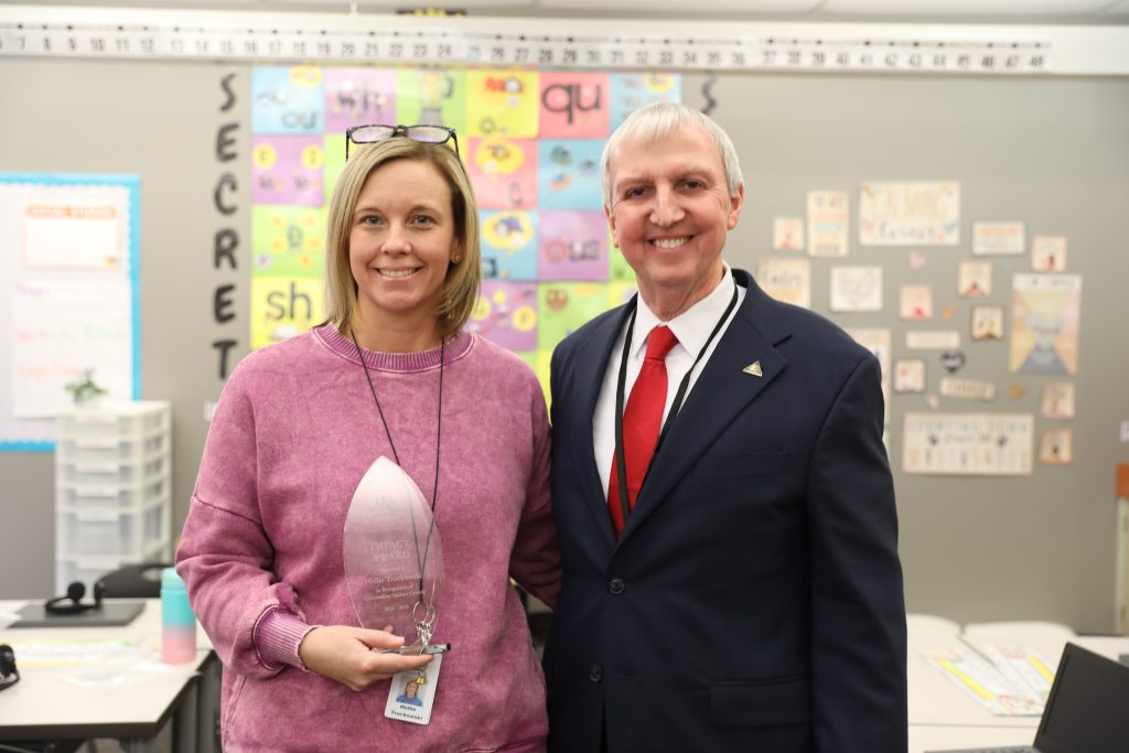 woman in pink sweatshirt with award standing next to man in black suit
