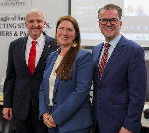 Woman in suit smiling, standing with men in suits