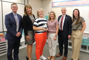 People standing and smiling, teacher holding award