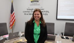 Woman standing in front of a podium at a conference table.