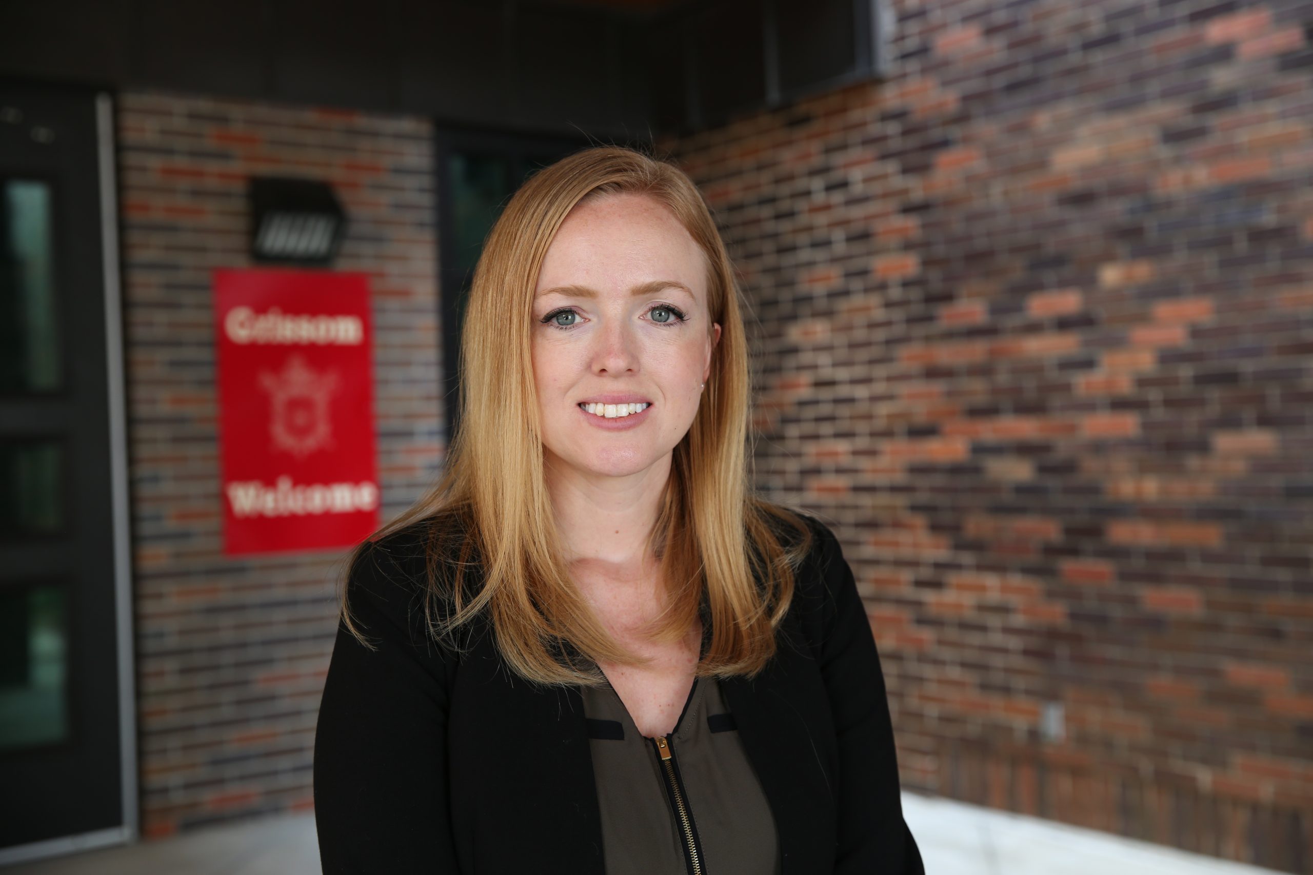 Woman standing in front of brick building, smiling at camera.