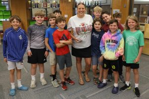 A group of students wearing colorful t-shirts and sweatshirts standing with their teacher in a classroom.