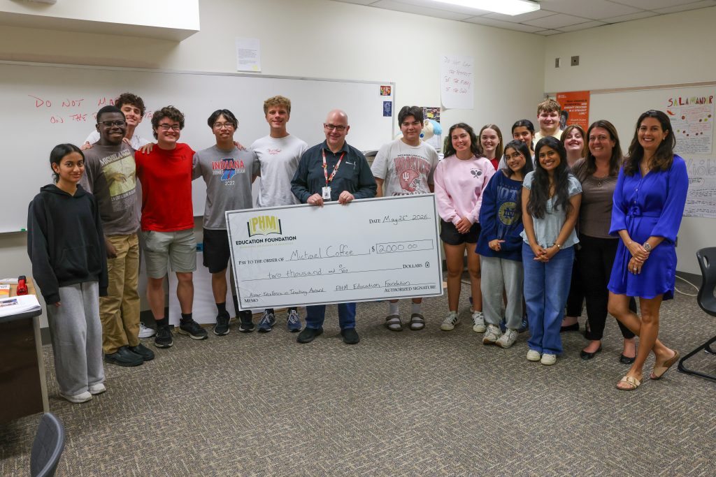 A group of people posing in a classroom setting, some holding a check, celebrating an achievement.