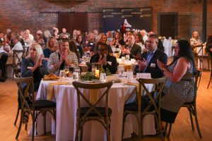 People gathered at a wedding reception in a large room, clapping and celebrating.