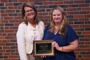 Two women holding a plaque in front of a brick wall.