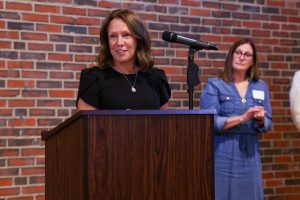 Two women standing at a podium during a formal event. One woman is speaking while the other listens attentively.