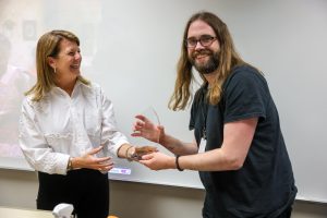 A woman laughing hands a man with long hair an award