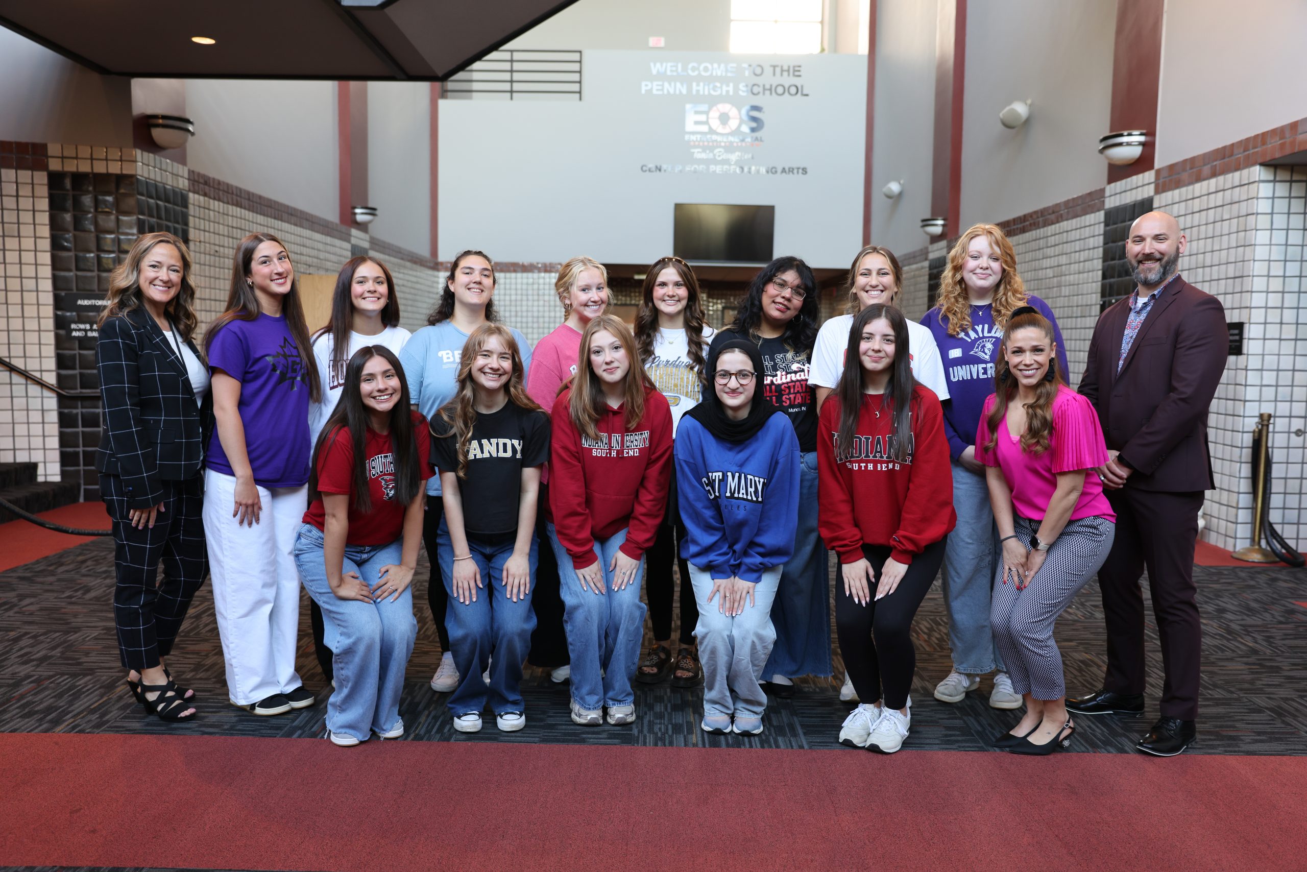 Group of young women posing for a photo in front of a school building, smiling and standing close together.