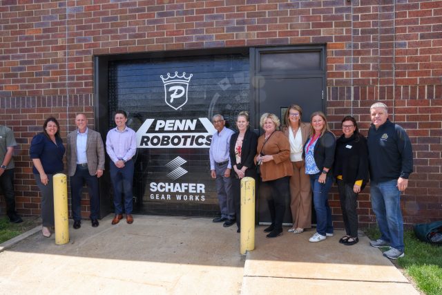 Group of people posing in front of a building with a sign that reads "PENN ROBOTICS" and a logo for Schaefer.