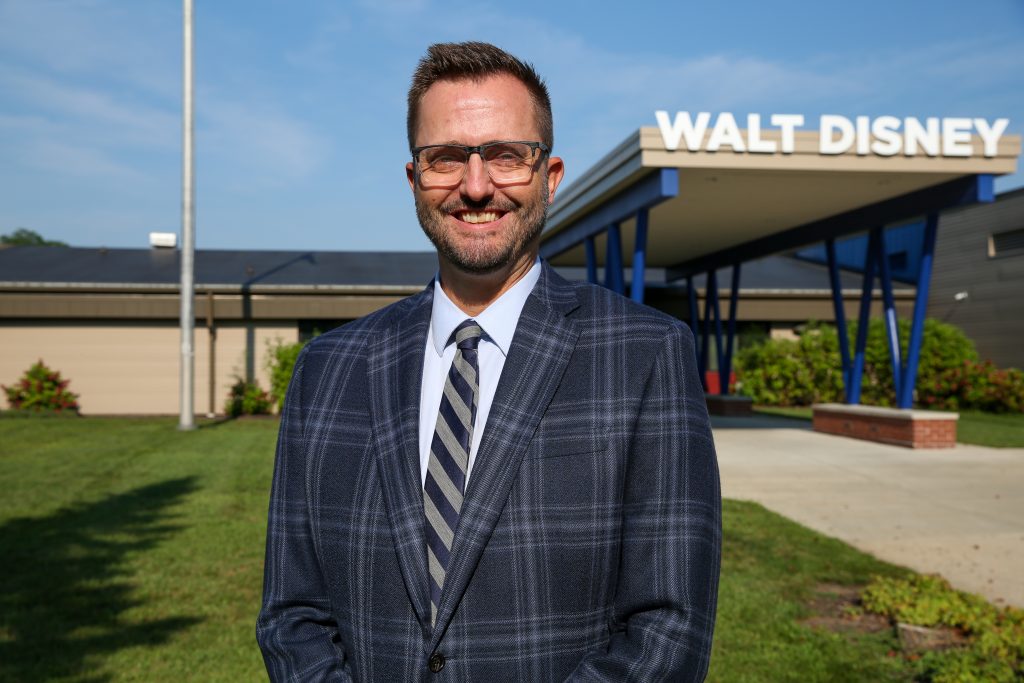 Man in suit standing in front of a sign that says "Walt Disney".