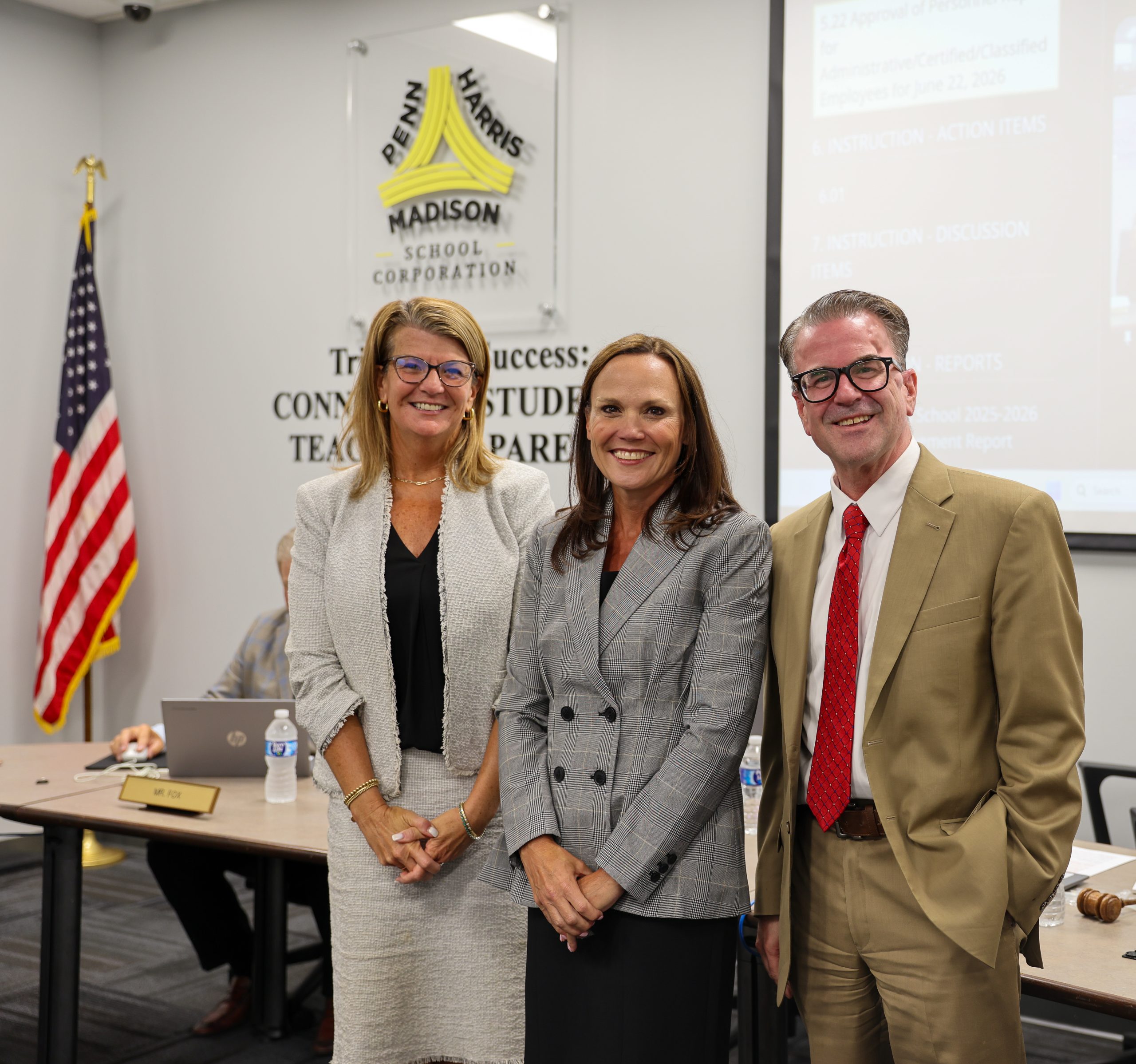 Three people standing in front of a podium at an event. The person on the left is wearing glasses and a red top. The middle