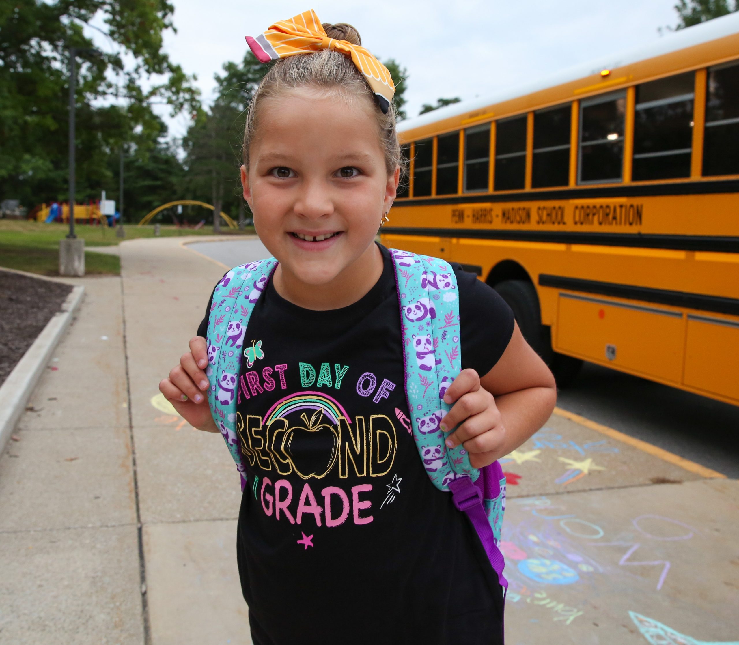 Girl in school uniform standing next to a yellow school bus.