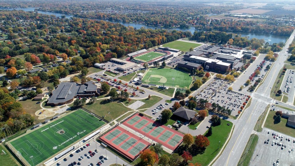 This is an aerial view of a Penn's campus during autumn. The campus is surrounded by trees with fall colors, and there's a river in the background