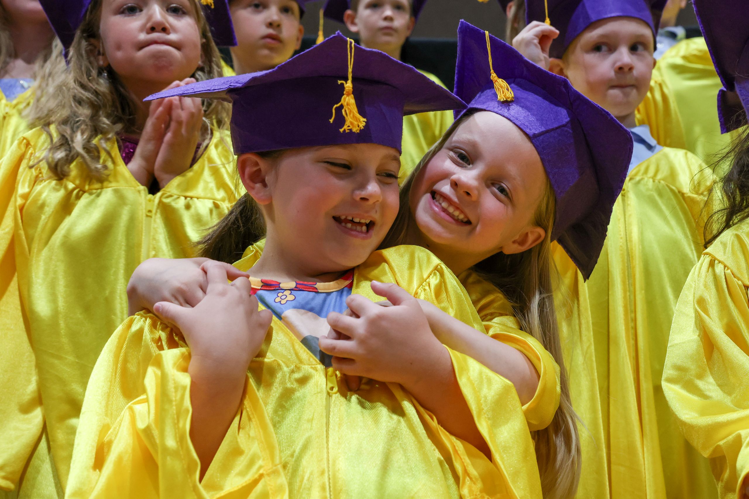 Young elementary children in graduation caps and gowns posing for a picture.