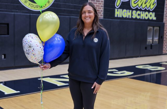 Woman in sports jersey holding balloons, smiling at camera, standing on basketball court.