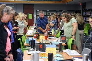 People gathered around tables in a library setting, engaged in conversation and activities, possibly during an event or