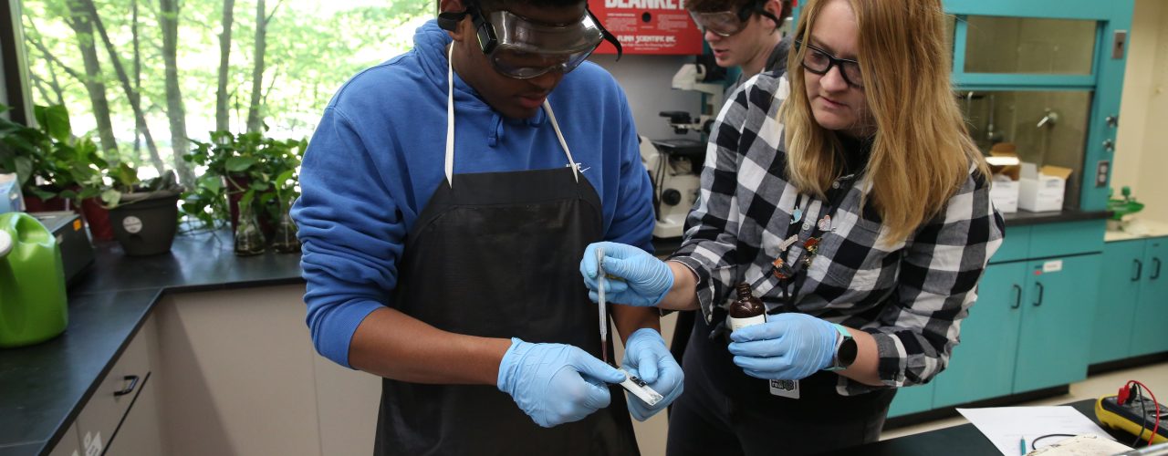 Two people in a lab setting, one wearing glasses, working on a project together.