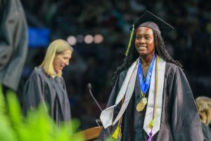 Woman in graduation cap and gown standing on stage holding a medal.