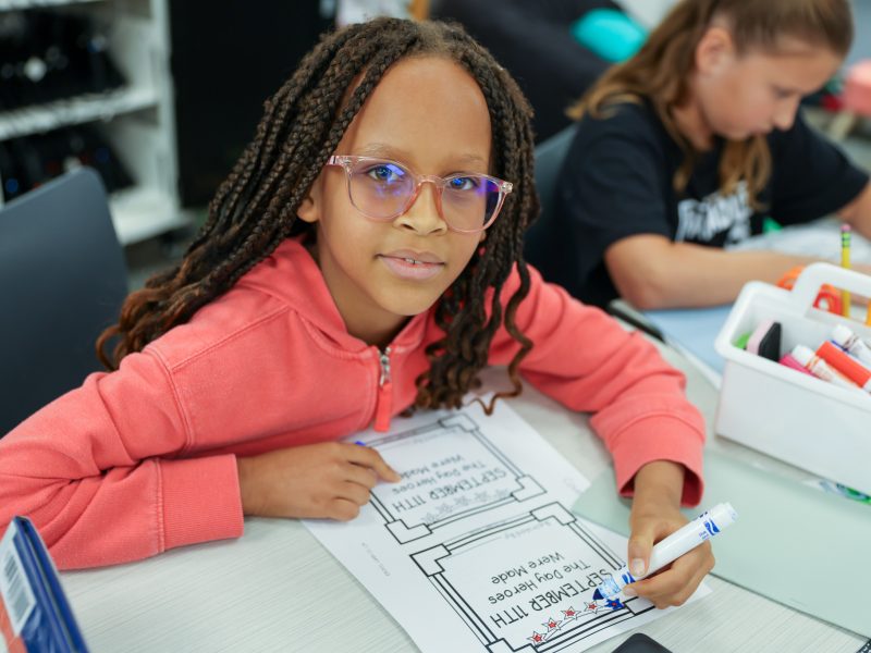 A young girl proudly holds up a sign in a classroom setting.