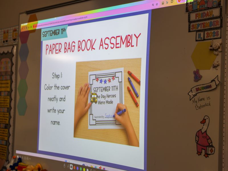 A young girl proudly holds up a handmade sign in a classroom setting.