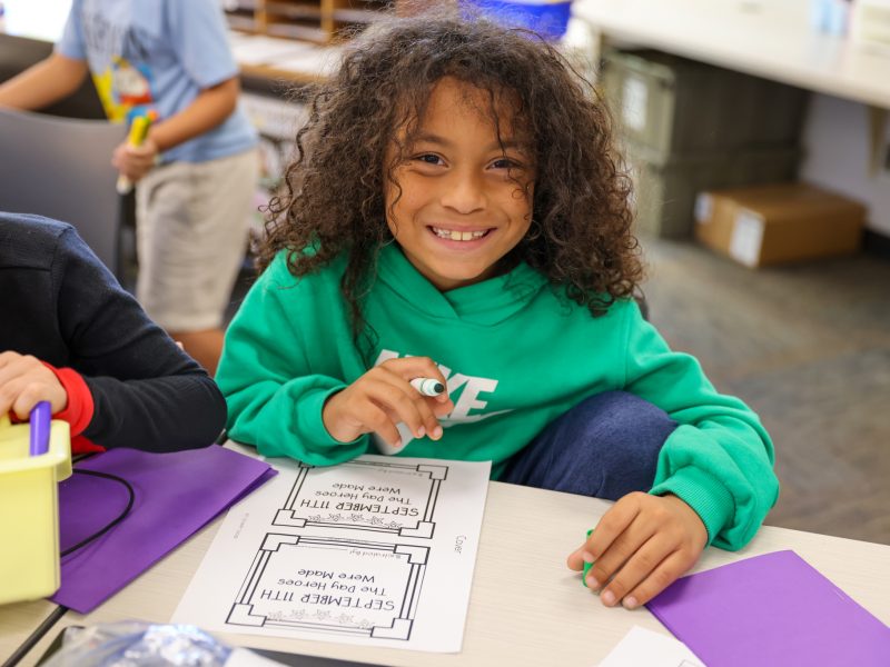 Girl holding a sign in front of a classroom.