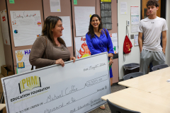 Woman presenting a check to two people in front of a classroom display. The check is from Phm Education Foundation and is