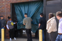Group of people standing in front of a closed business, looking at a large black tarp covering the entrance.
